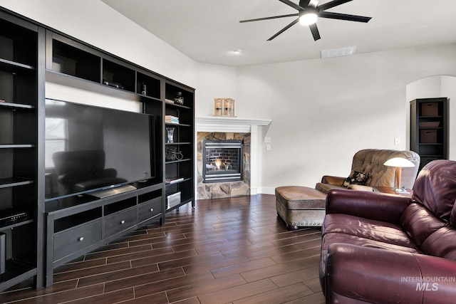 living room featuring a stone fireplace, wood finish floors, visible vents, and a ceiling fan