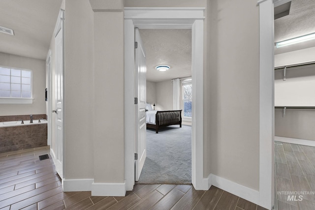 corridor with a textured ceiling, wood finish floors, visible vents, and baseboards