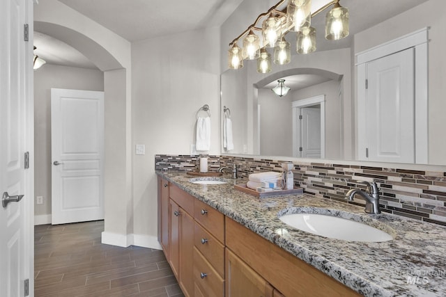 bathroom featuring baseboards, wood finished floors, a sink, and decorative backsplash