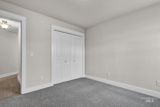 unfurnished bedroom with dark colored carpet, a closet, and baseboards