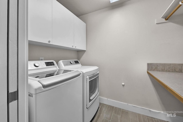 laundry area with wood finish floors, independent washer and dryer, cabinet space, and baseboards