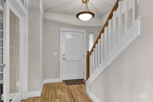 foyer featuring light wood finished floors, stairway, and baseboards