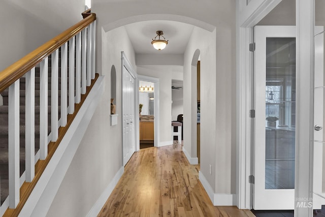 hallway with arched walkways, light wood-style flooring, and baseboards