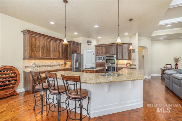 11954 W Meadowfalls Dr, Star, ID 83669 - kitchen with appliances with stainless steel finishes, a spacious island, arched walkways, a kitchen bar, and dark wood finished floors
