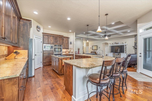 11954 W Meadowfalls Dr, Star, ID 83669 - kitchen featuring a large island with sink, dark wood finished floors, appliances with stainless steel finishes, a ceiling fan, and coffered ceiling