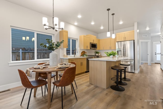 kitchen featuring pendant lighting, light brown cabinets, light hardwood / wood-style floors, and appliances with stainless steel finishes