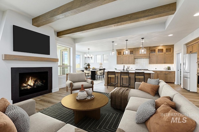 6998 S Tindaris Ave, Meridian, ID 83642 - living area featuring light wood-style flooring, recessed lighting, a chandelier, beamed ceiling, and a lit fireplace