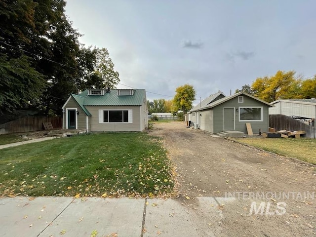 view of front of house with metal roof, driveway, a front lawn, and fence