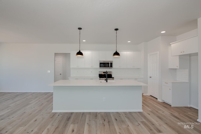 kitchen featuring a center island with sink, white cabinets, light hardwood / wood-style floors, and decorative light fixtures