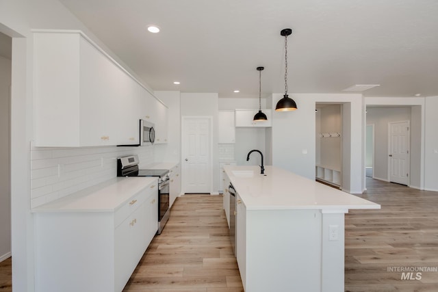 kitchen featuring sink, hanging light fixtures, stainless steel appliances, white cabinets, and a center island with sink