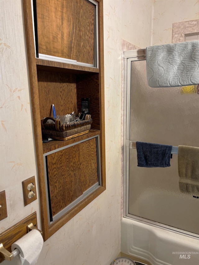 bathroom featuring enclosed tub / shower combo and a textured wall