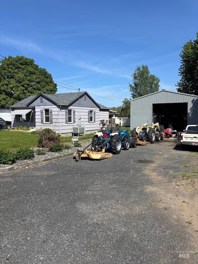 view of front of house featuring a detached garage, an outdoor structure, roof with shingles, and cooling unit