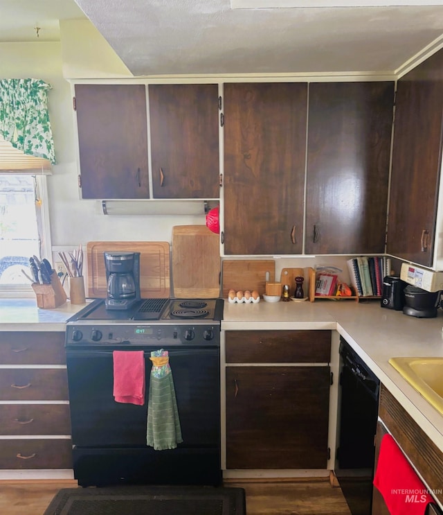 kitchen with black appliances, light countertops, dark brown cabinets, and wood finished floors