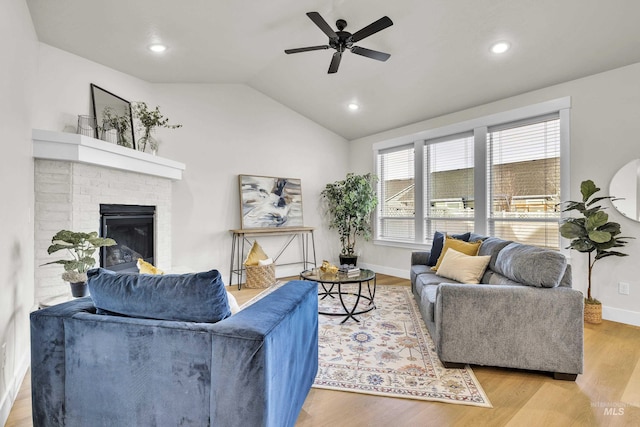 living room featuring a fireplace, light hardwood / wood-style floors, vaulted ceiling, and ceiling fan