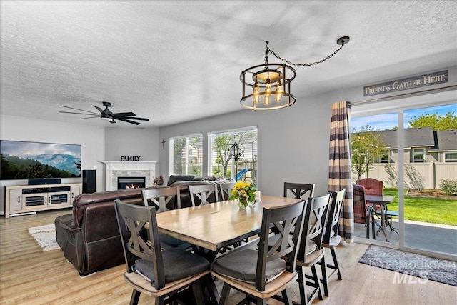 4226 E Tahiti St, Meridian, ID 83646 - dining room with light wood finished floors, a lit fireplace, a textured ceiling, a chandelier, and ceiling fan