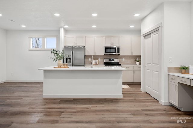 kitchen with appliances with stainless steel finishes, light wood-type flooring, and a center island with sink