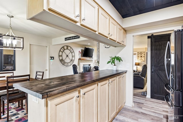 kitchen with light hardwood / wood-style floors, stainless steel refrigerator, light brown cabinetry, hanging light fixtures, and a barn door