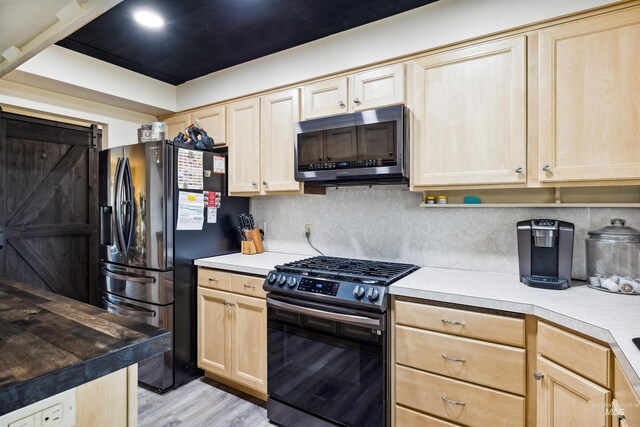 kitchen with fridge with ice dispenser, light brown cabinetry, a barn door, and black gas range oven