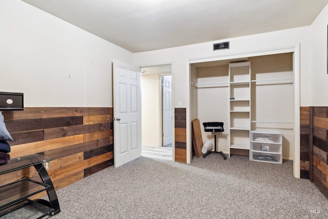 carpeted bedroom featuring wood walls and a closet