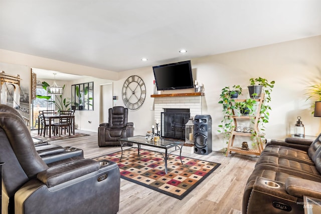 living room with a brick fireplace, light wood-type flooring, and a chandelier