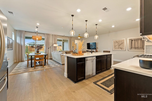 kitchen with stainless steel dishwasher, decorative light fixtures, dark brown cabinets, a center island with sink, and light wood-type flooring