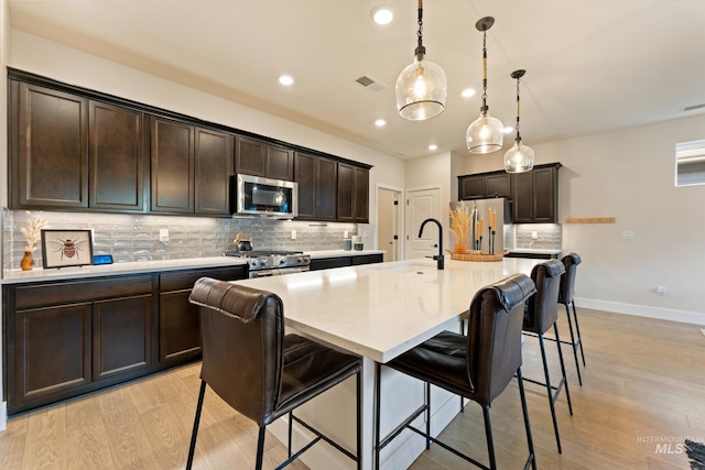 kitchen featuring a center island with sink, light wood-type flooring, hanging light fixtures, and appliances with stainless steel finishes