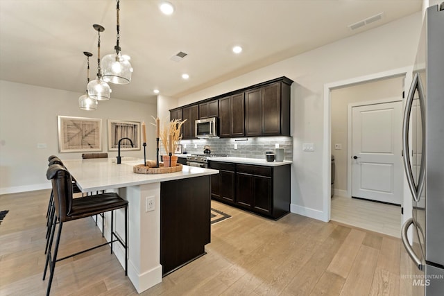 kitchen with a kitchen island with sink, hanging light fixtures, light wood-type flooring, a kitchen bar, and stainless steel appliances