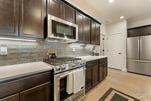 kitchen featuring decorative backsplash, appliances with stainless steel finishes, light hardwood / wood-style floors, and dark brown cabinets