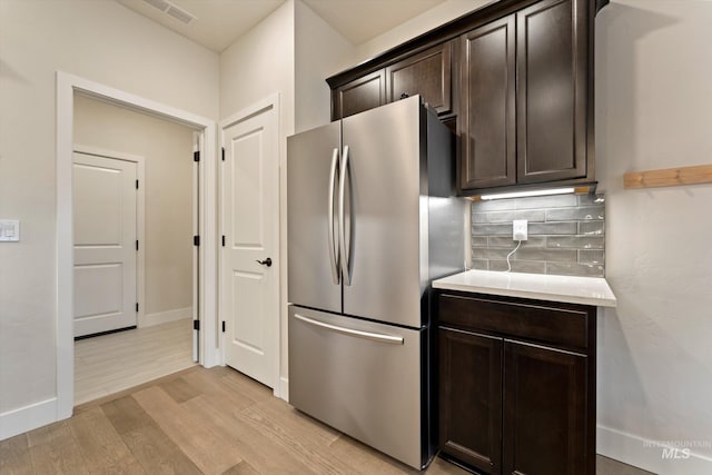 kitchen featuring stainless steel fridge, dark brown cabinetry, light hardwood / wood-style floors, and backsplash