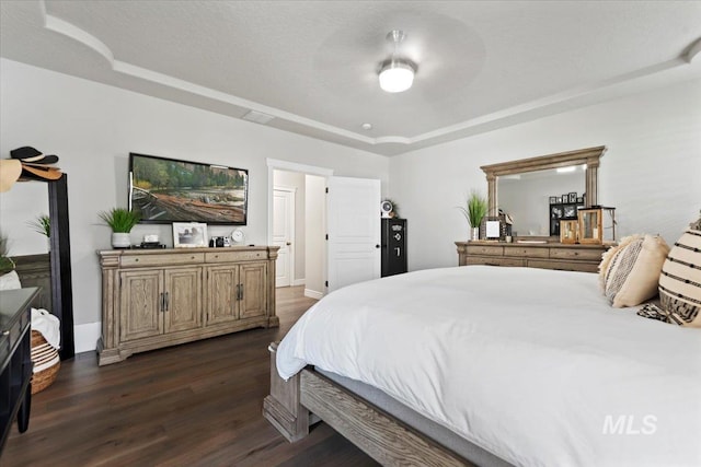 bedroom with a textured ceiling, a tray ceiling, and dark wood-style flooring