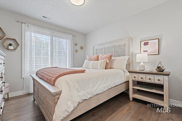 bedroom with a textured ceiling, dark wood-style flooring, visible vents, and baseboards