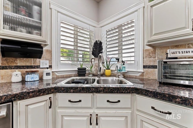 kitchen featuring a toaster, a sink, white cabinets, backsplash, and glass insert cabinets