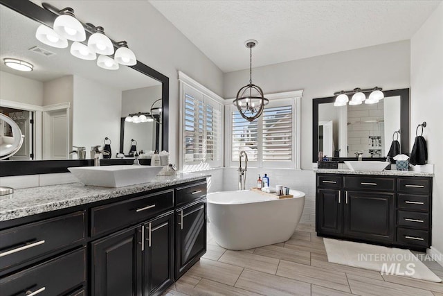 bathroom featuring visible vents, a sink, a textured ceiling, and a freestanding bath