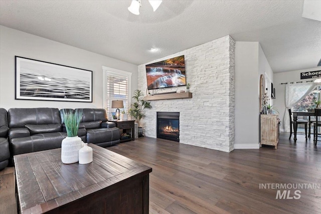 living room featuring a textured ceiling, baseboards, dark wood-style flooring, and a stone fireplace