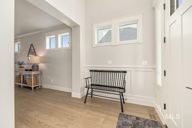 living area featuring a wainscoted wall, crown molding, visible vents, a decorative wall, and wood finished floors