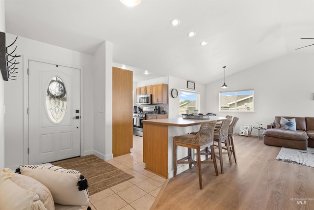 kitchen featuring a kitchen breakfast bar, vaulted ceiling, hanging light fixtures, appliances with stainless steel finishes, and open floor plan