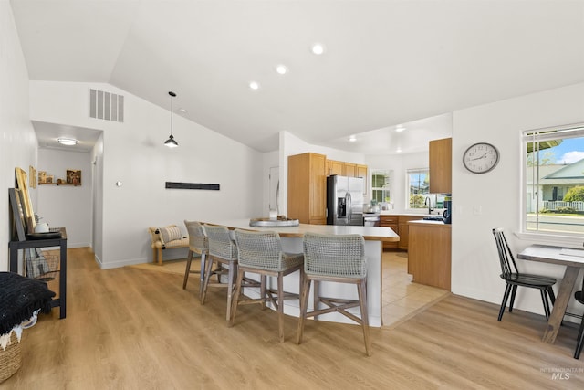 kitchen with stainless steel refrigerator with ice dispenser, vaulted ceiling, visible vents, and plenty of natural light