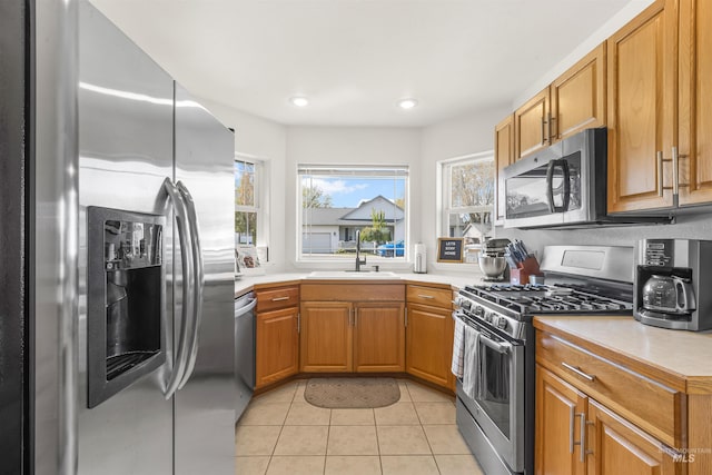 kitchen featuring a sink, brown cabinetry, light tile patterned floors, stainless steel appliances, and light countertops