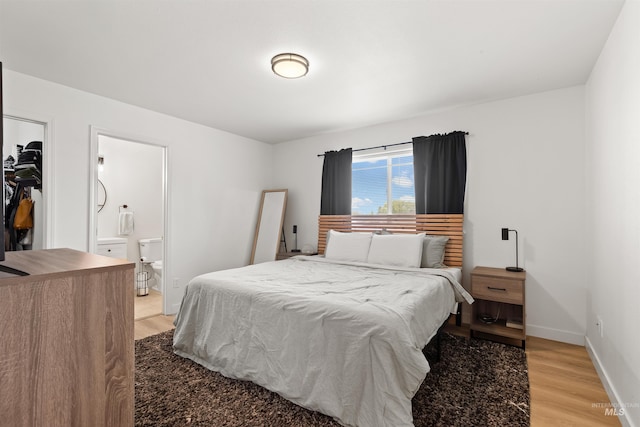 bedroom with a spacious closet, ensuite bathroom, light wood finished floors, and a closet