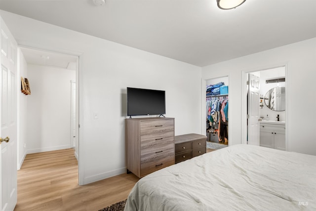 bedroom featuring a closet, a spacious closet, attic access, light wood-style flooring, and baseboards