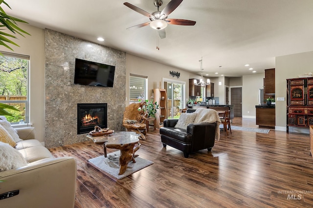 living room featuring ceiling fan with notable chandelier, hardwood / wood-style flooring, a tiled fireplace, baseboards, and recessed lighting