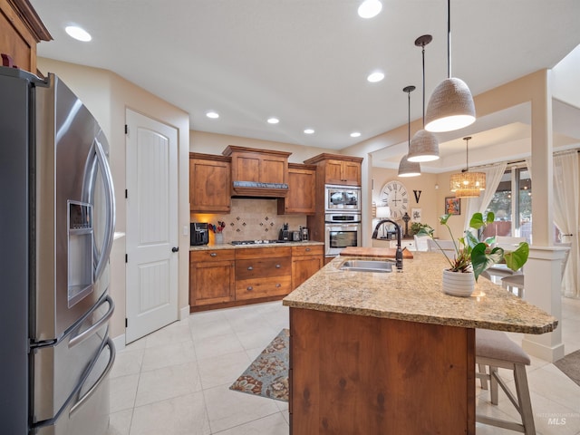 kitchen with a kitchen bar, sink, light stone counters, hanging light fixtures, and appliances with stainless steel finishes