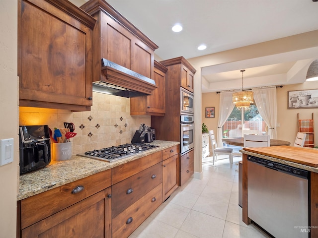 kitchen with pendant lighting, premium range hood, stainless steel appliances, light tile patterned flooring, and decorative backsplash