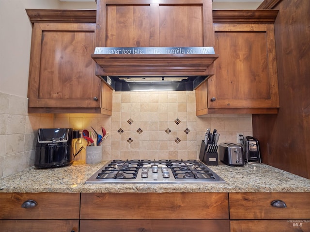 kitchen featuring premium range hood, stainless steel gas cooktop, light stone counters, and backsplash