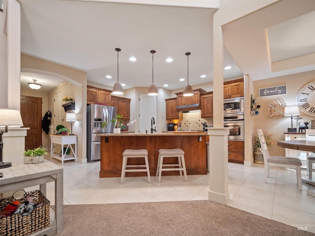 kitchen featuring a breakfast bar, hanging light fixtures, a kitchen island with sink, light tile patterned floors, and stainless steel appliances