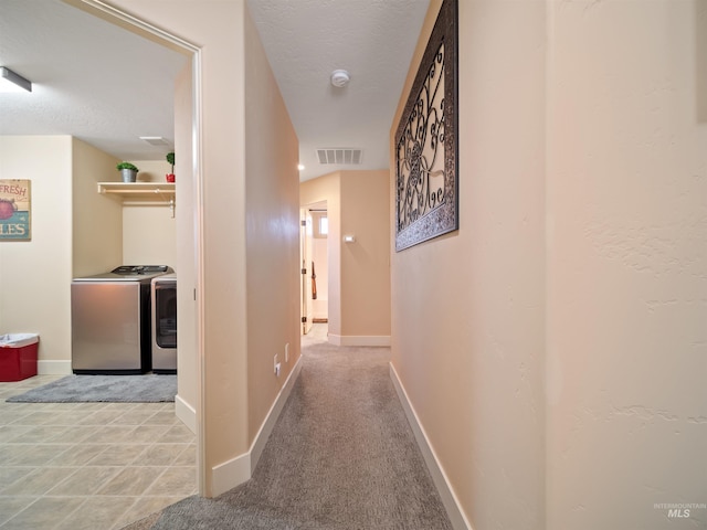 hall featuring light carpet, a textured ceiling, and washer and clothes dryer