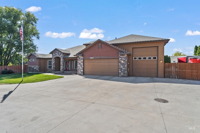 view of front of house with a garage, driveway, stone siding, and fence