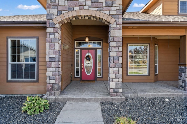 doorway to property with stone siding and a shingled roof