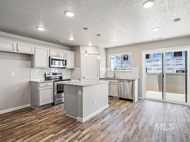 kitchen featuring a center island, dark hardwood / wood-style floors, a textured ceiling, decorative light fixtures, and stainless steel appliances