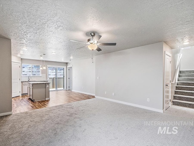 unfurnished living room with ceiling fan, sink, light hardwood / wood-style floors, and a textured ceiling